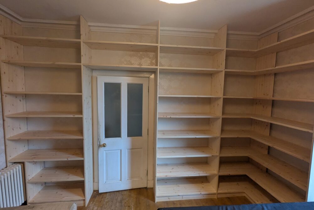 Beautiful wooden built-in bookshelves by Abernethy Joinery installed on two walls surrounding a door in a room, with empty shelves and a radiator visible on the left. Perfect for any Perth home seeking timeless storage solutions.