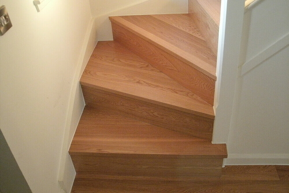 A skilled carpenter in Perth crafted this wooden staircase with angled steps that turn sharply to the right, bordered by white walls and a handrail on the upper section near Abernethy.